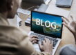 man typing on laptop with blog on screen